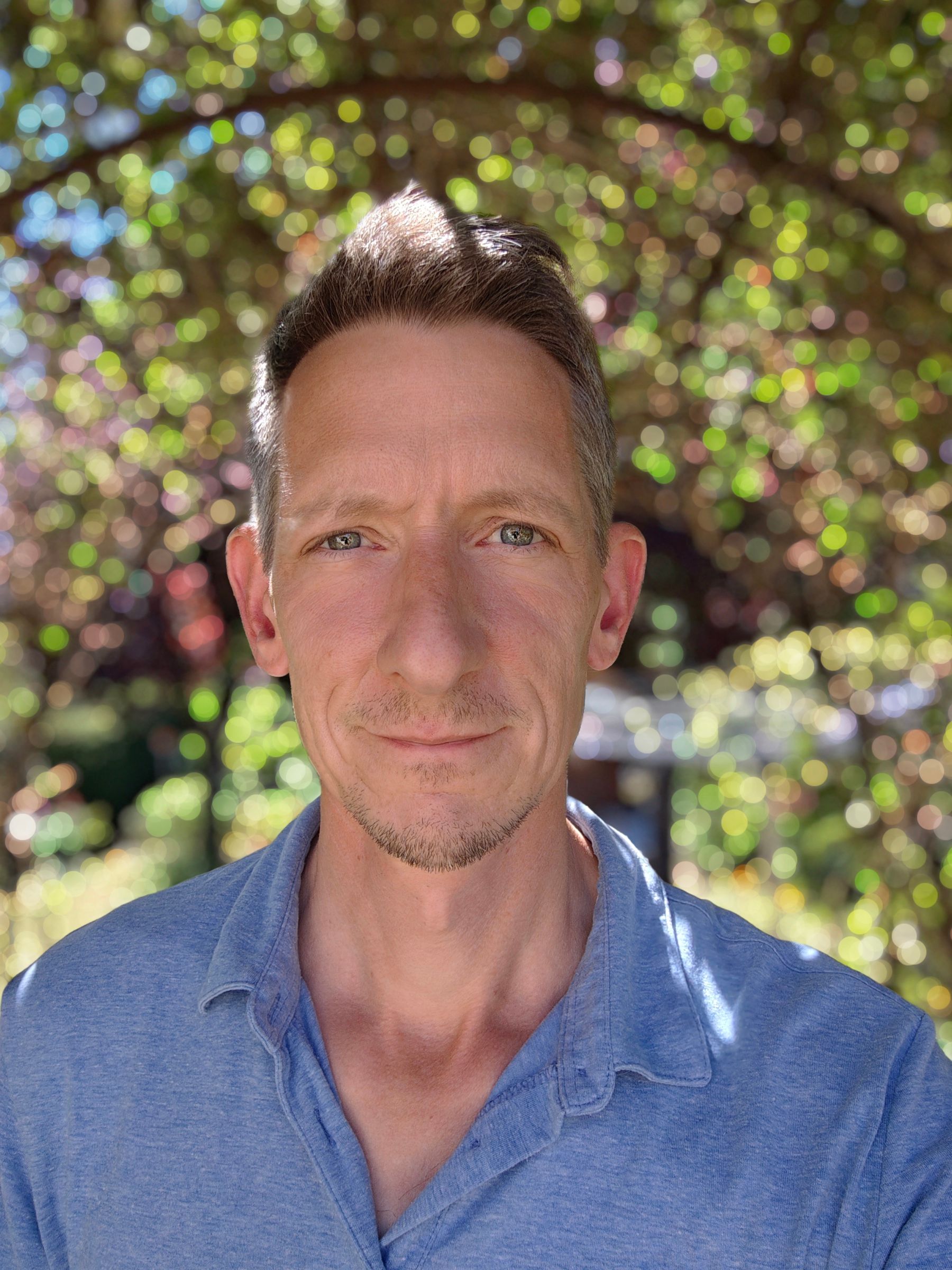 Philippe Ramakers lächelt unter einem Blätterdach, im Hintergrund Sonnenlicht